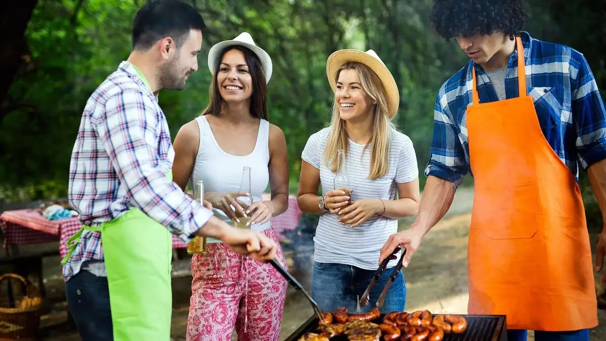 Friends laughing and eating around a grill.