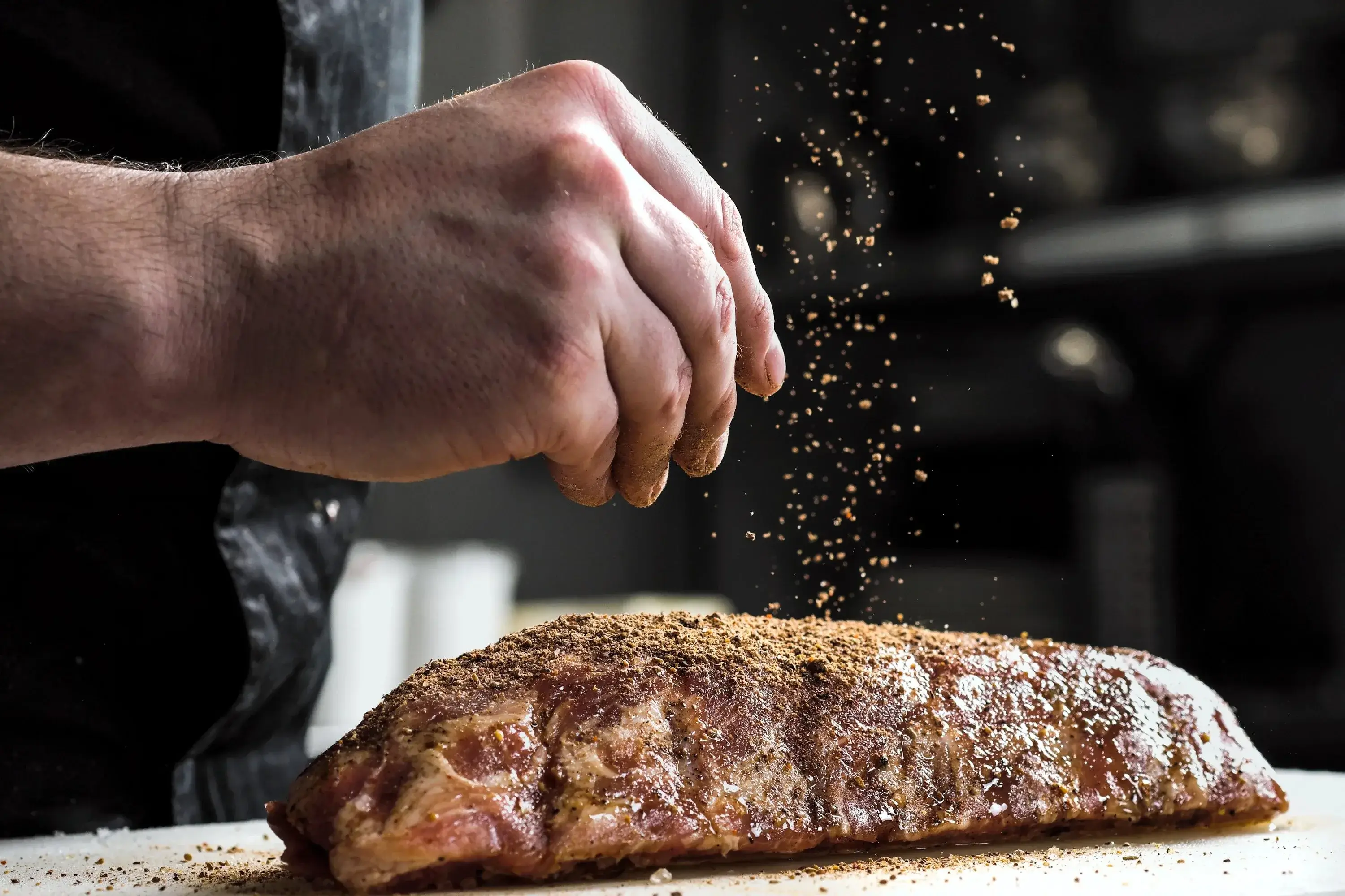 A chef's hands carefully seasoning a piece of meat before grilling.